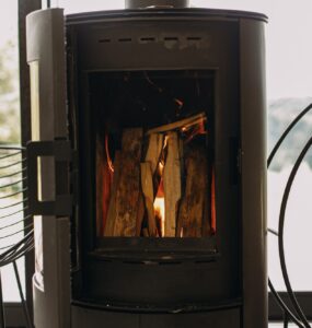Modern black fireplace with burning fire and firewood on metal stand. Cozy warm moments