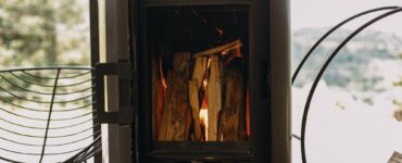 Modern black fireplace with burning fire and firewood on metal stand. Cozy warm moments