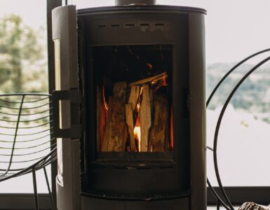 Modern black fireplace with burning fire and firewood on metal stand. Cozy warm moments