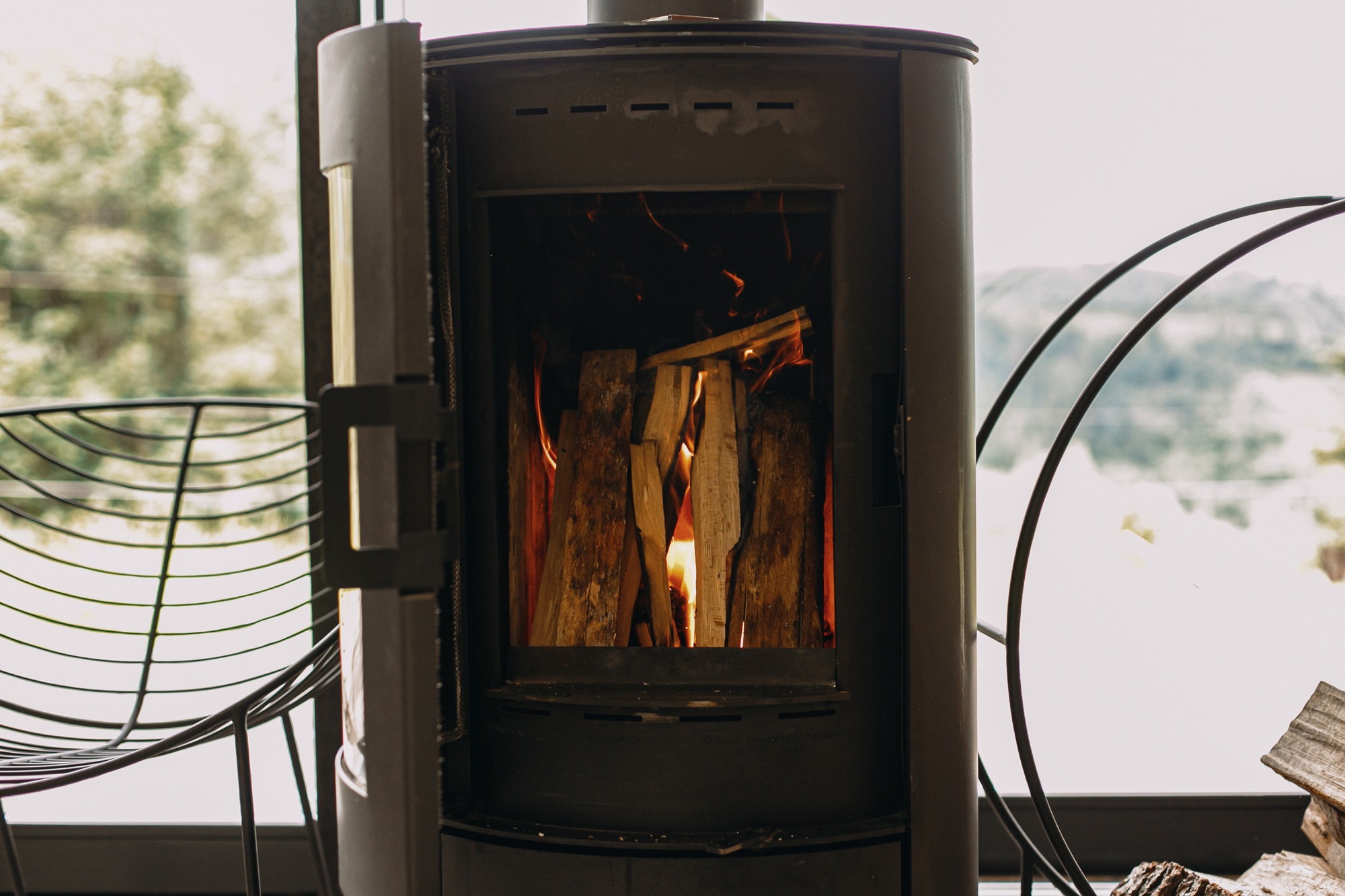 Modern black fireplace with burning fire and firewood on metal stand. Cozy warm moments