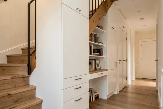 Rangement sous escalier sur mesure avec armoires blanches laquées, tiroirs intégrés et espace bureau dans un appartement moderne