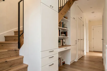 Rangement sous escalier sur mesure avec armoires blanches laquées, tiroirs intégrés et espace bureau dans un appartement moderne